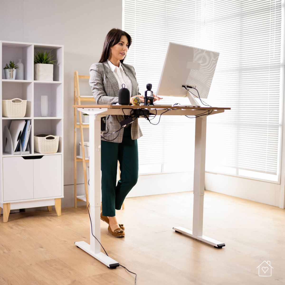 Woman working at a height-adjustable standing desk beside window blinds that reduce screen glare.