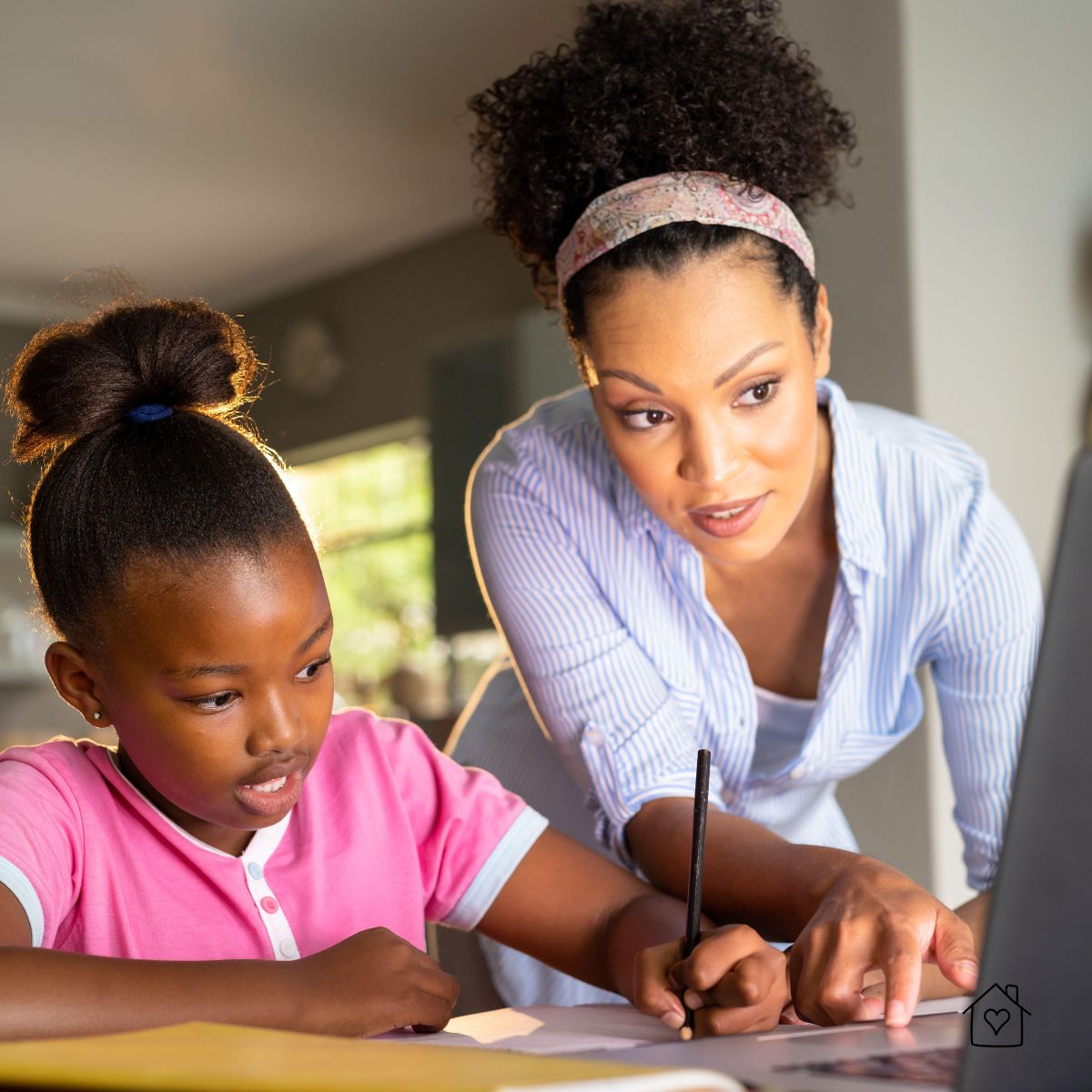 Mother helping her daughter with writing at home, pointing to a laptop screen during a homeschool essay lesson.