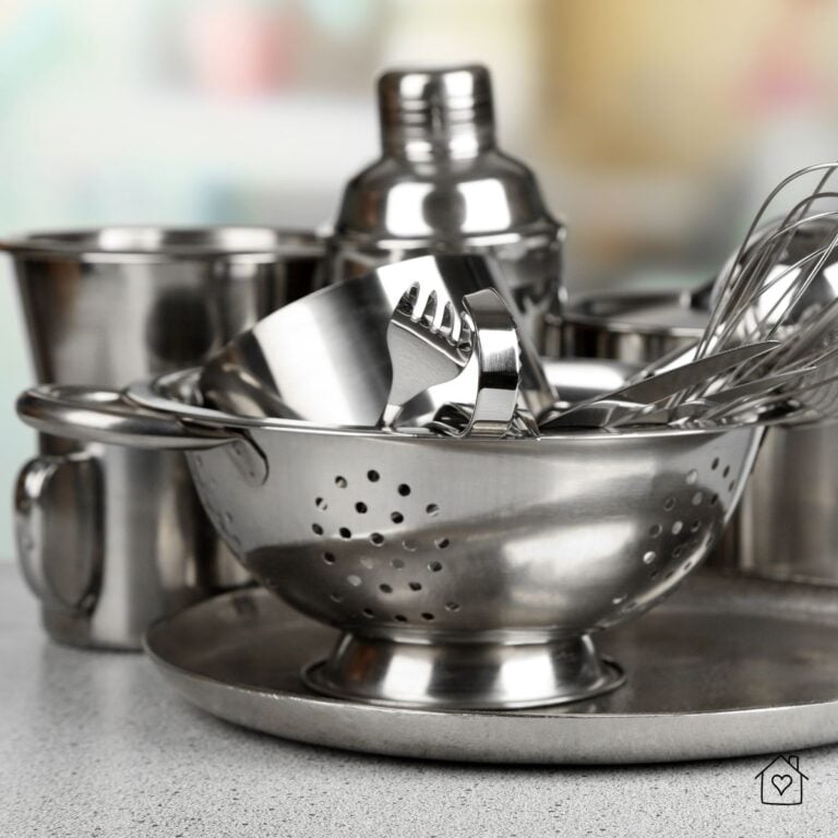 A close-up of stainless steel kitchen utensils including a whisk, measuring cups, and a colander arranged neatly on a countertop.