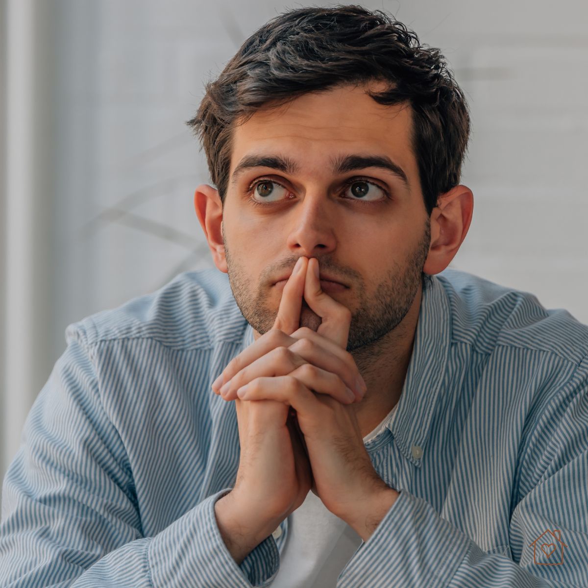 Pensive man gazing upward, hands together, illustrating rumination.