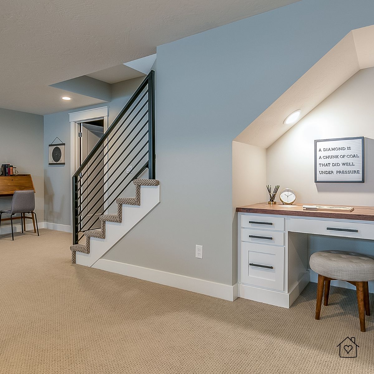 Small basement workspace tucked beneath a staircase, featuring a white built-in desk, soft lighting, and a motivational wall quote for a functional home office nook.