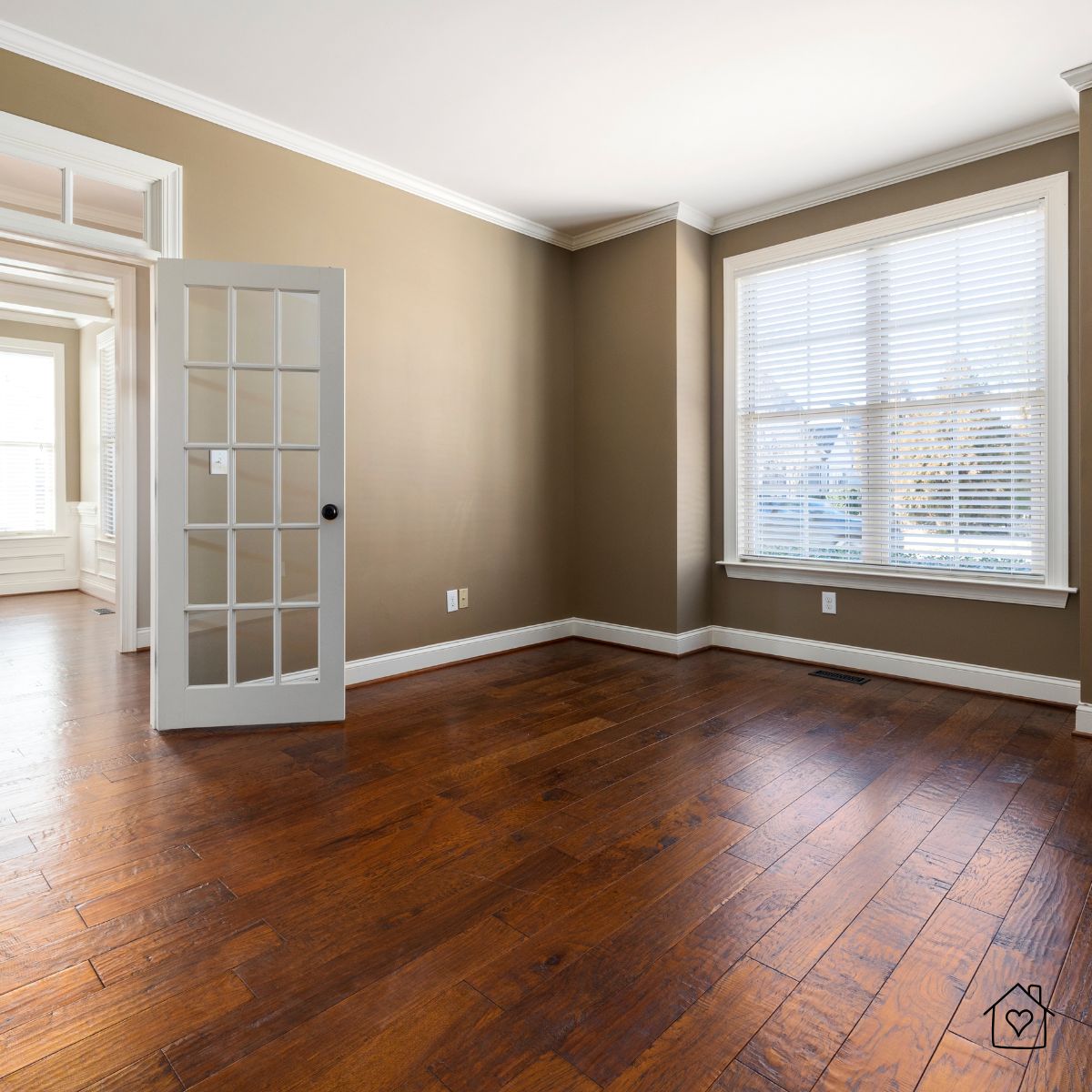 Empty room with natural light and visible wear on hardwood flooring near the window area.