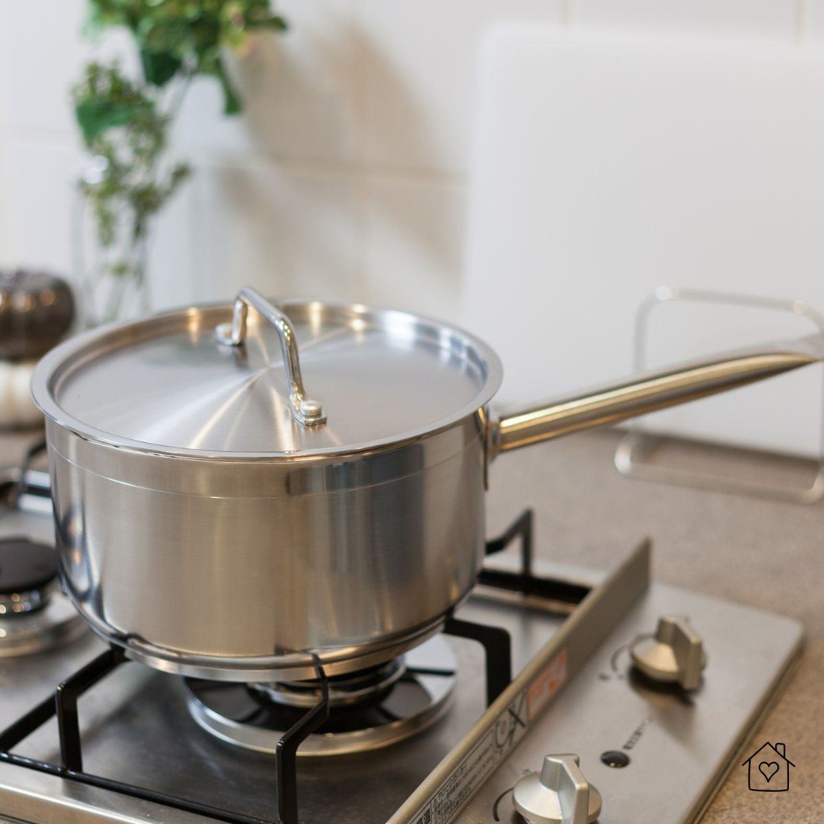 A stainless steel saucepan with a lid placed on a gas stove, ready for cooking in a clean kitchen setting.