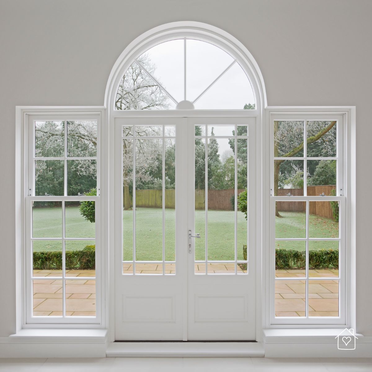 Interior view of white French doors with tall sidelights and an arched transom, demonstrating how larger panes and patio doors increase daylight in living spaces.