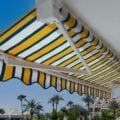 Premium retractable awning with blue and yellow stripes shading a balcony near the coast