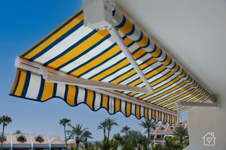 Premium retractable awning with blue and yellow stripes shading a balcony near the coast