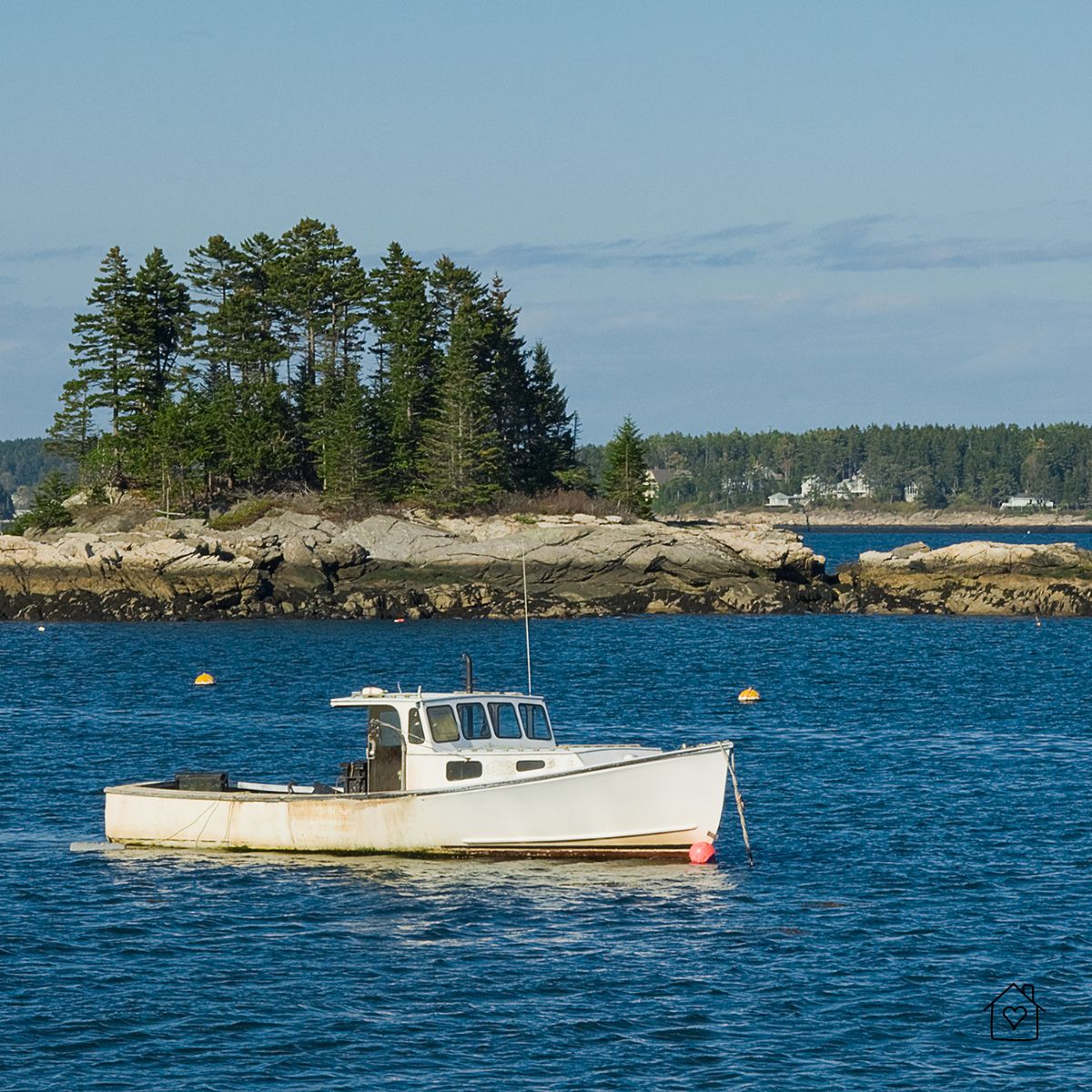 A small white lobster boat floating near a rocky island with pine trees along the Maine coastline.