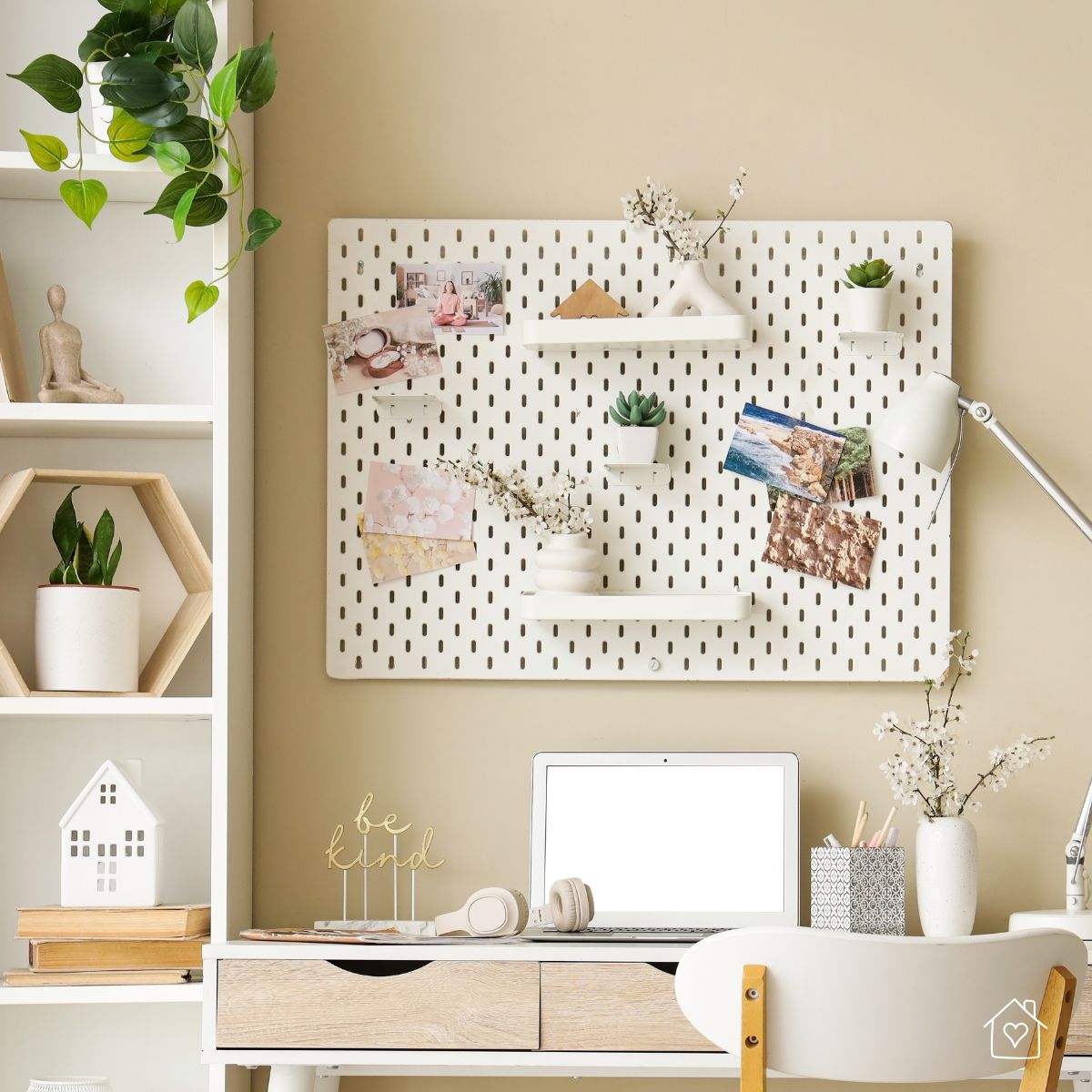 White pegboard above a small desk holding shelves, plants, and notes for simple, space-saving storage.