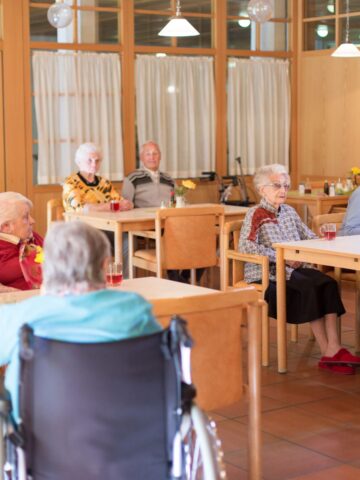 Group of senior residents sitting together in a nursing home dining room, illustrating community life and social interaction in long-term care facilities.