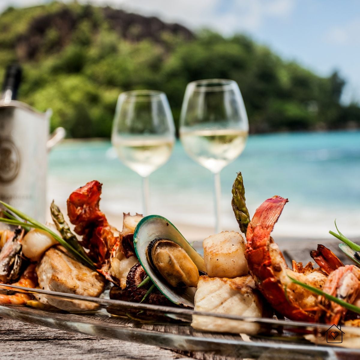 A grilled seafood platter with lobster, mussels, and scallops paired with white wine on a beachside table.