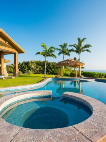 Resort-style pool overlooking the ocean with palm trees and spa area, symbolizing relaxation and easy living.