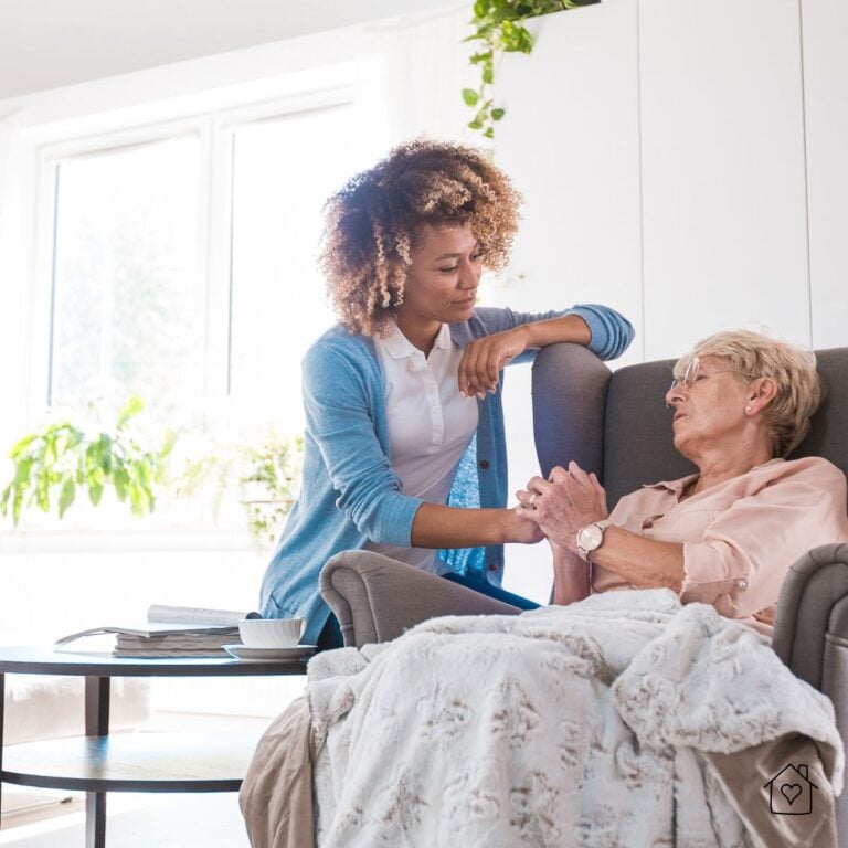 Caregiver holding hands with an older woman in a cozy home environment, demonstrating emotional support and comfort for senior residents.