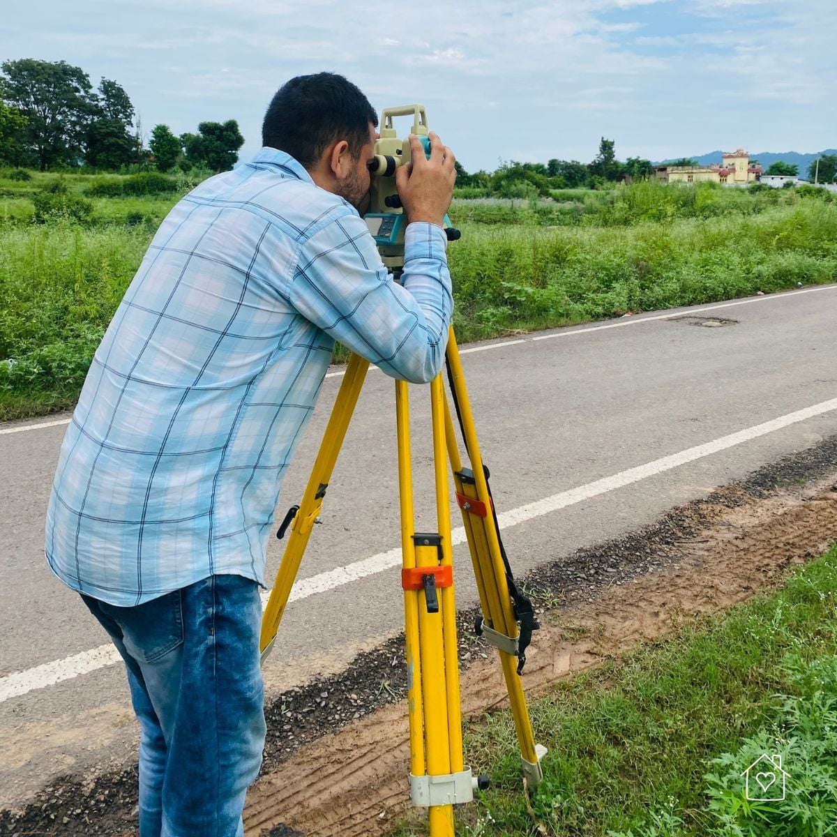 Field surveyor using a theodolite on a tripod near a roadway to capture elevations and site control points.