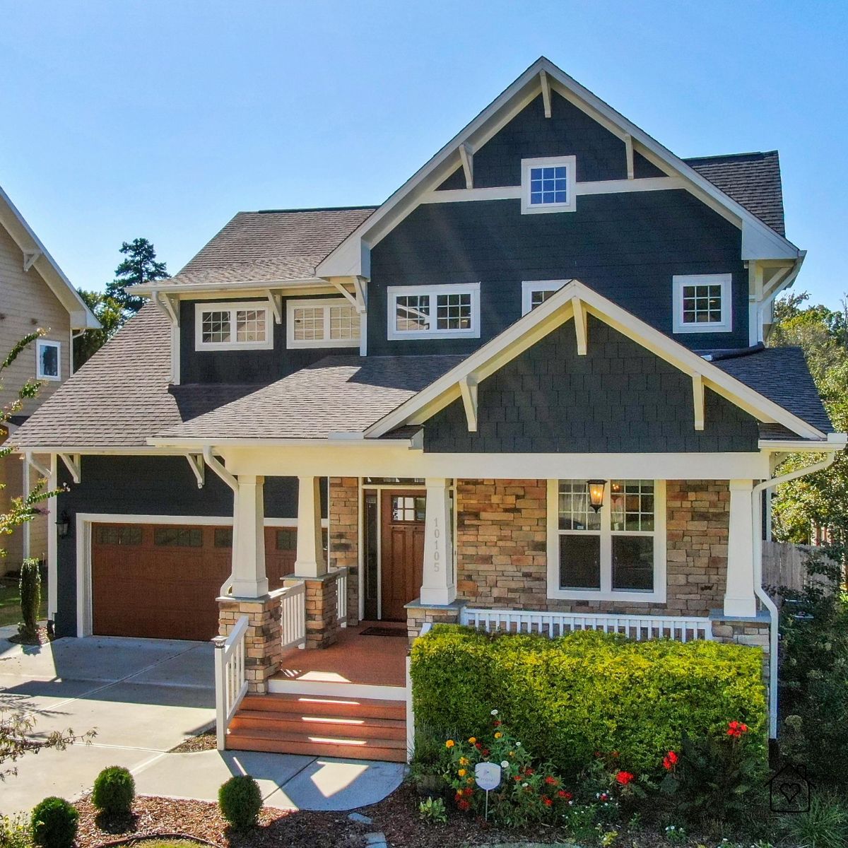 Front elevation of a completed custom home with dark cladding, stone accents, and a timber door.