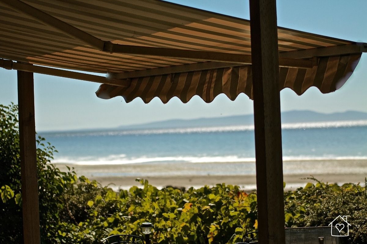 Taupe striped retractable awning shading a patio with ocean in the background