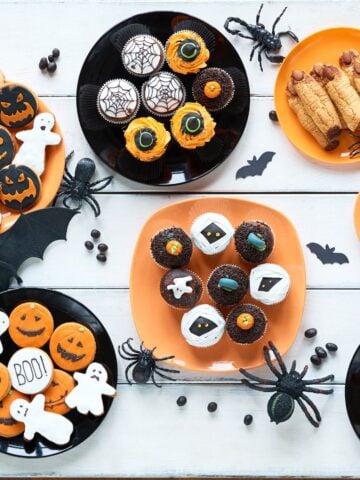 Assorted themed cupcakes, cookies, and candies arranged on orange and black plates. Reason: This wide, bright image gives an overview of multiple treats at once — perfect for attracting