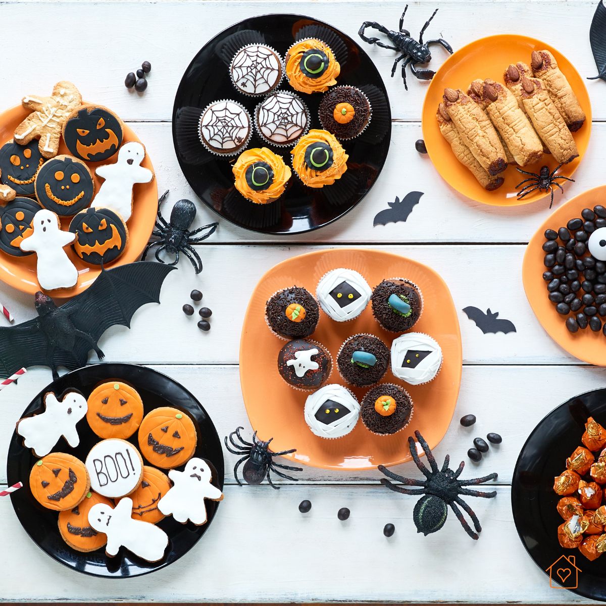 Assorted themed cupcakes, cookies, and candies arranged on orange and black plates. Reason: This wide, bright image gives an overview of multiple treats at once — perfect for attracting