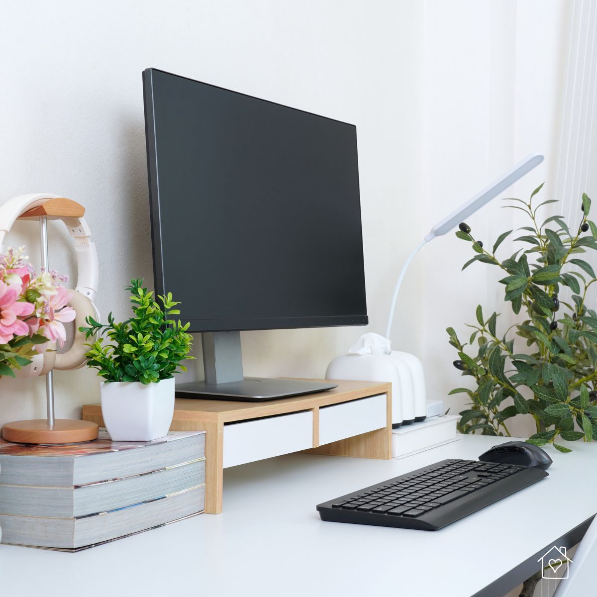 Minimal desktop with monitor on a small riser, slim task lamp, keyboard, and plants for a clean workspace.