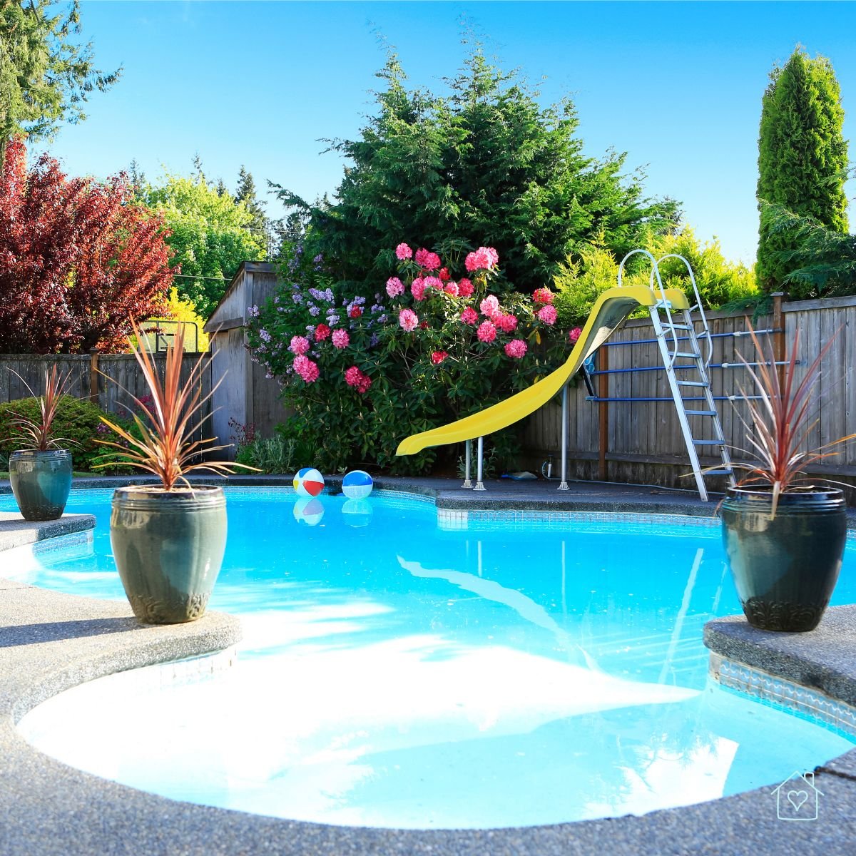 Fun backyard pool area featuring a yellow slide, potted plants, and vibrant pink flowers under bright blue sky.