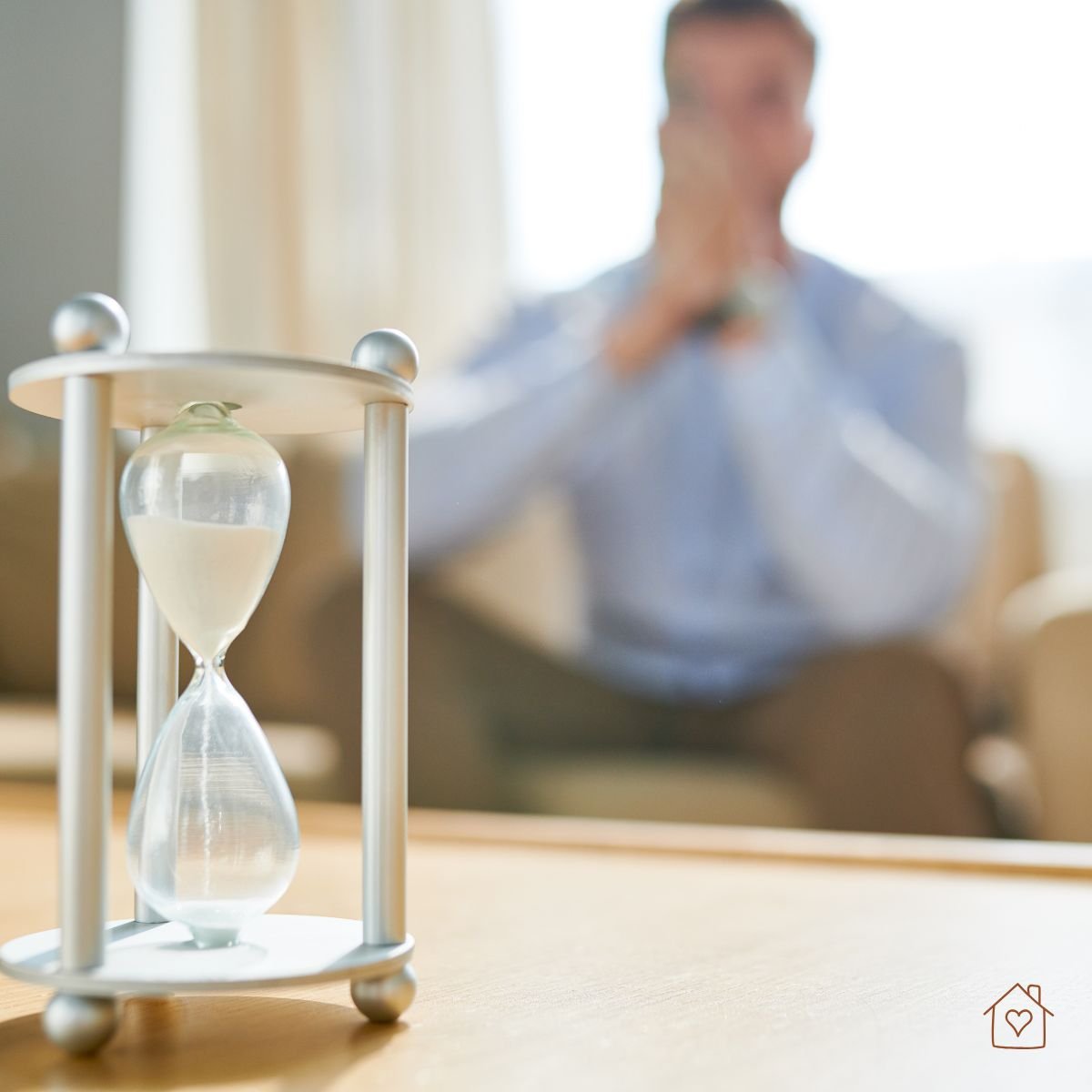 Hourglass on table with blurred person behind it, symbolizing a worry window.