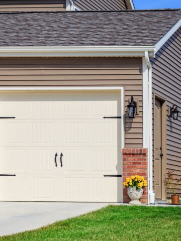 Brown vinyl-sided New Jersey home with white garage door and brick accents on a sunny day