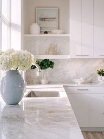 Bright white kitchen with large windows, marble counters, and minimal decor, highlighting smart design that lets natural light fill the room.