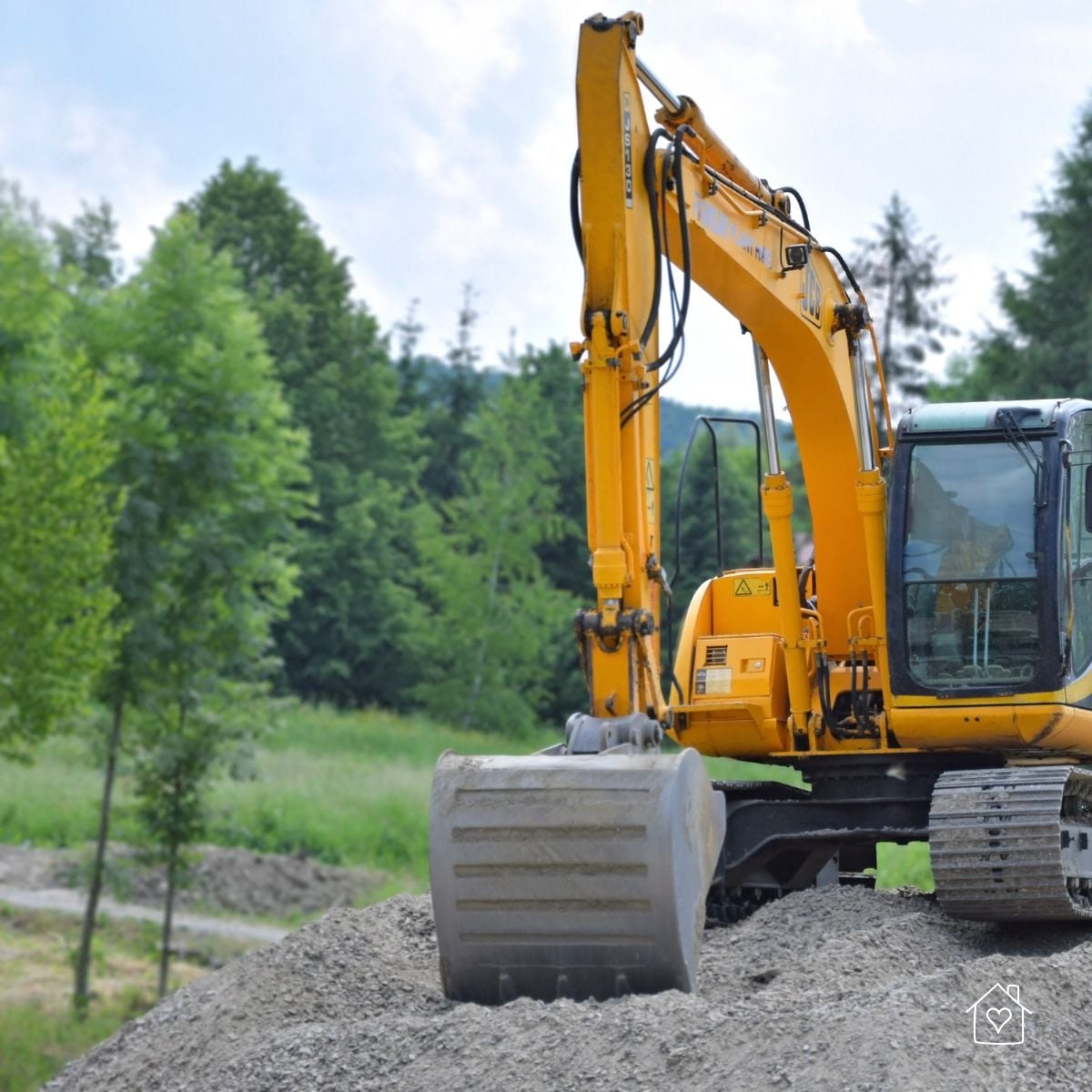 Excavator sitting on a gravel mound during grading, ready to spread and compact aggregate.