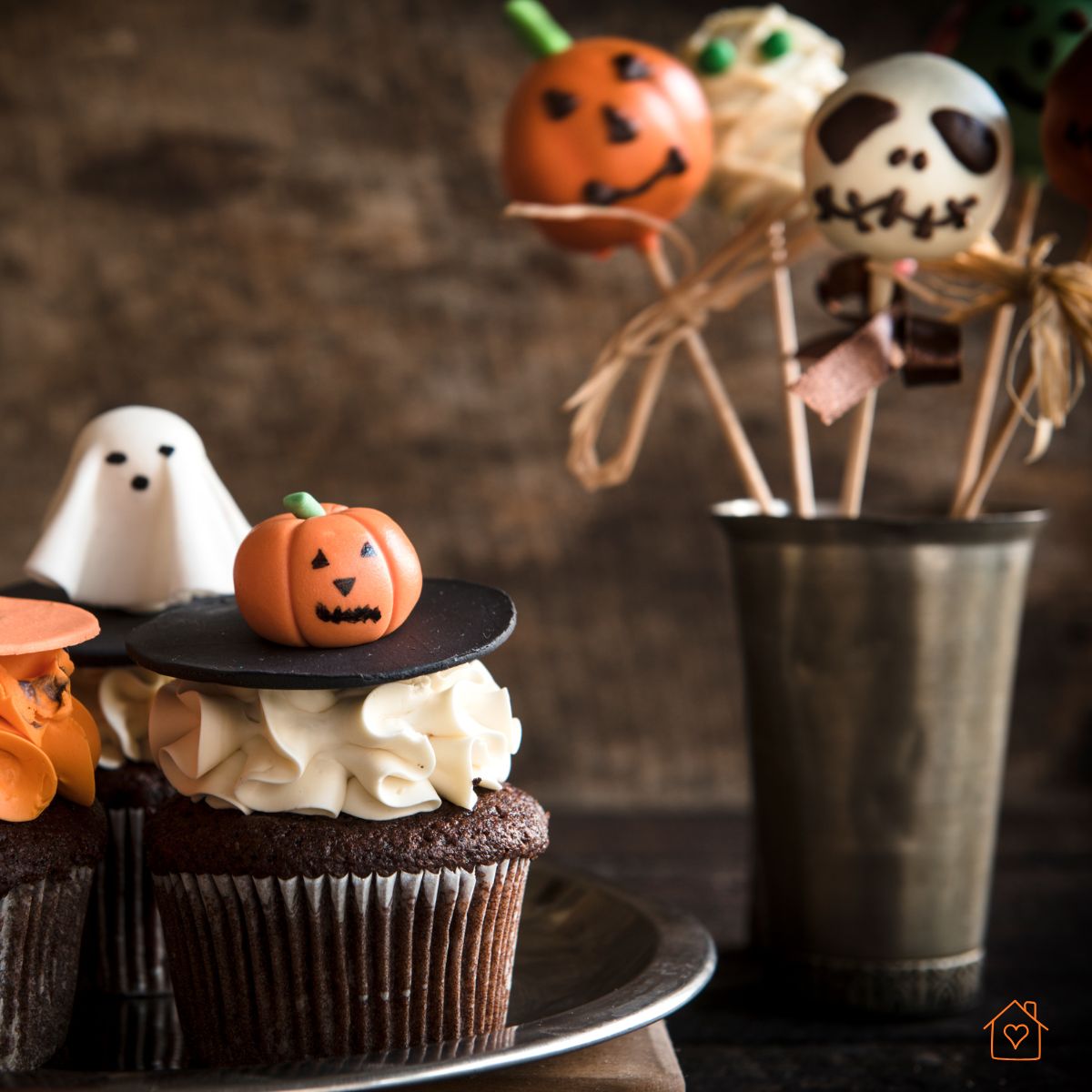 Cupcakes decorated with miniature pumpkins, ghosts, and themed cake pops on sticks.