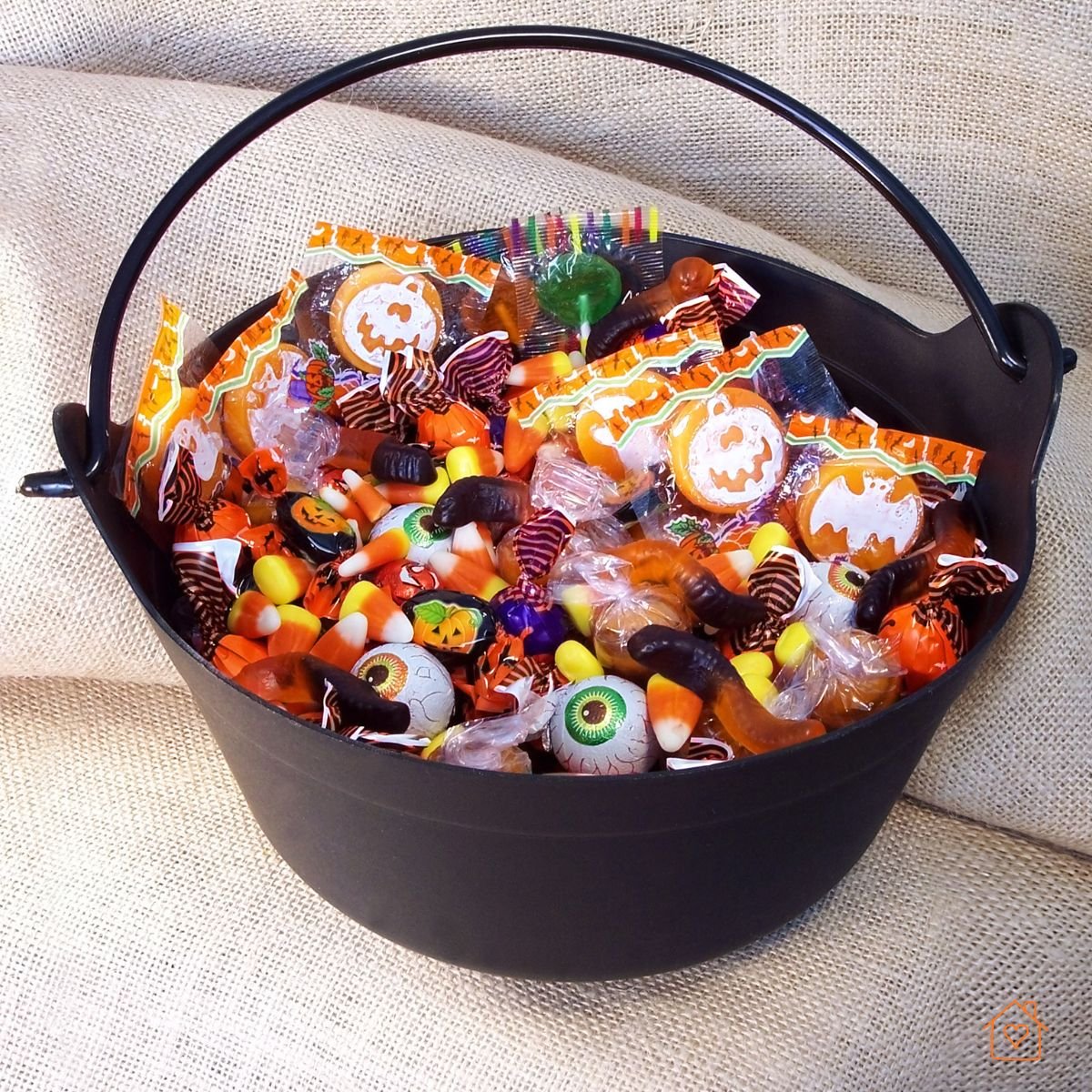 Black bucket filled with assorted wrapped candies, gummy worms, candy corn, and festive sweets.