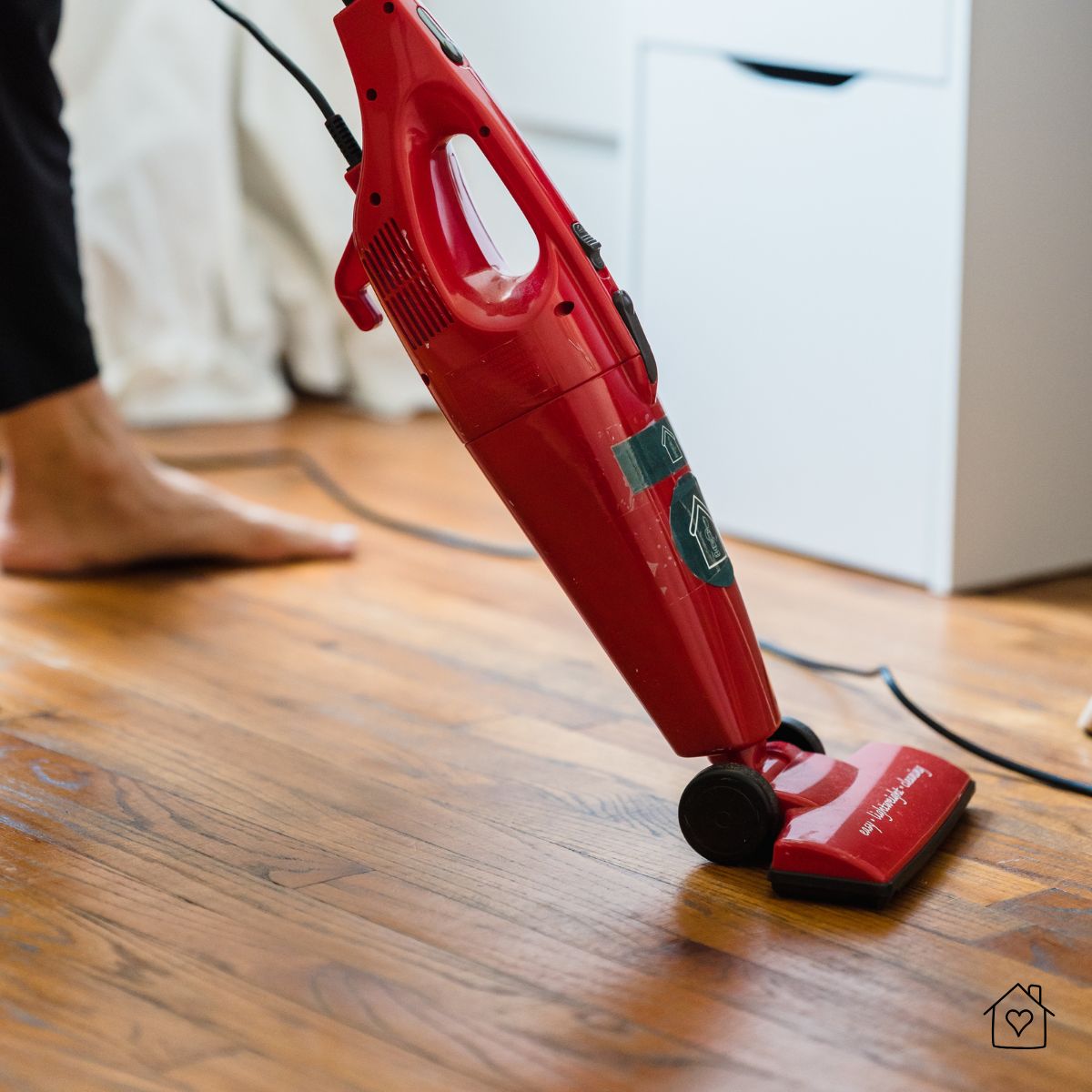 Red upright vacuum cleaner being used on hardwood flooring.