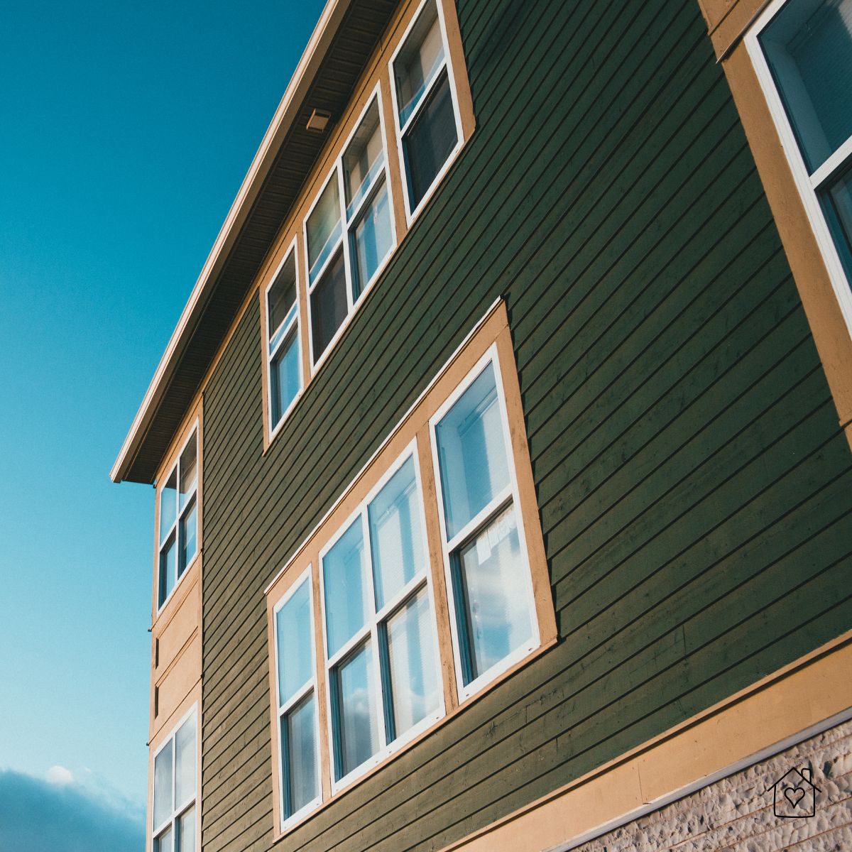 Two-story home with dark green lap siding and cream trim under blue sky