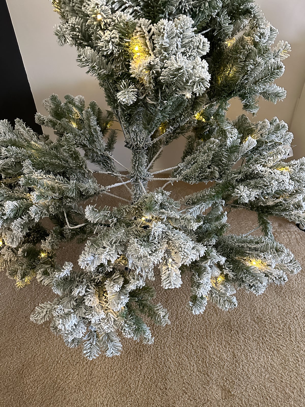 Close-up of flocked branches with warm white lights during setup.