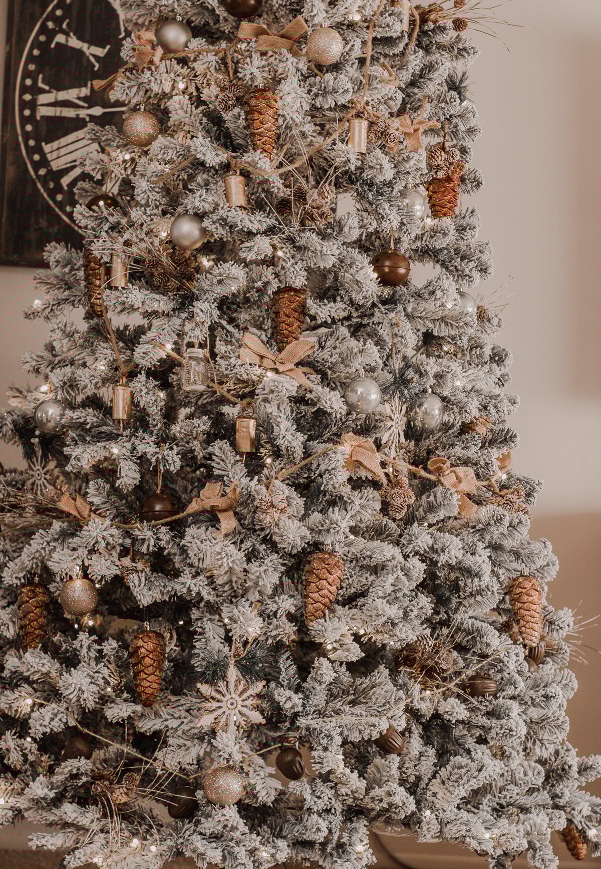 Bronze pinecones, champagne baubles, and burlap bows on a flocked branch.
