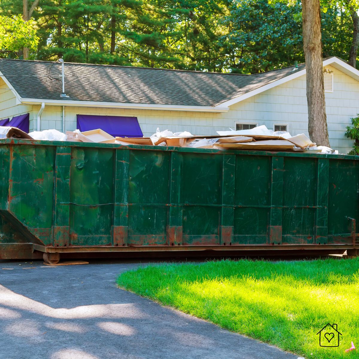 Large green roll-off dumpster on a driveway during a home renovation, filled with demo debris.