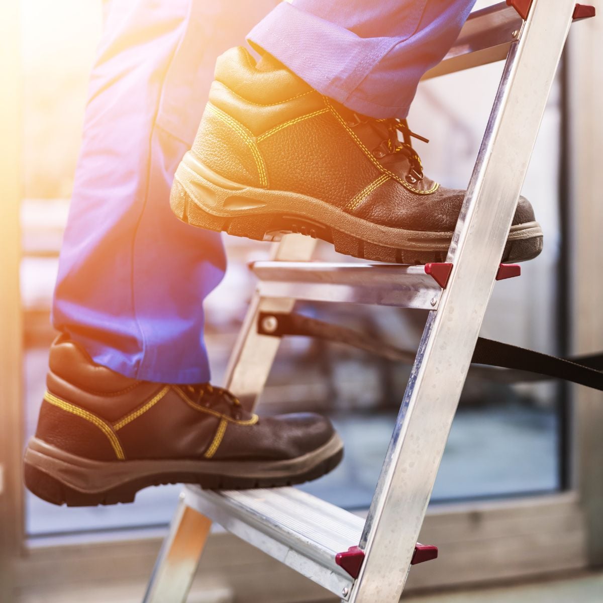 Worker wearing slip-resistant safety boots while climbing an aluminum ladder indoors.