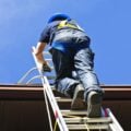 Person climbing an extension ladder to a roof while wearing a helmet and harness, demonstrating safe roof access.