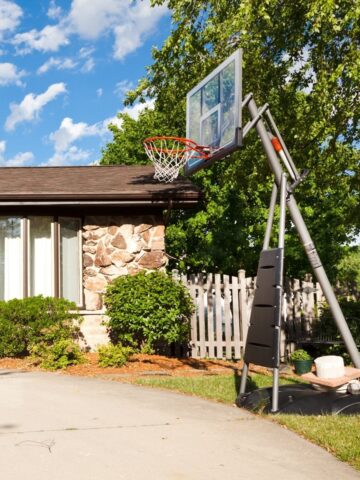 Portable basketball hoop on suburban driveway under blue sky