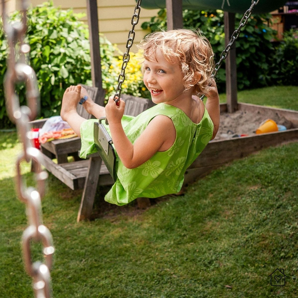 Smiling child on backyard swing with sandbox and toys behind