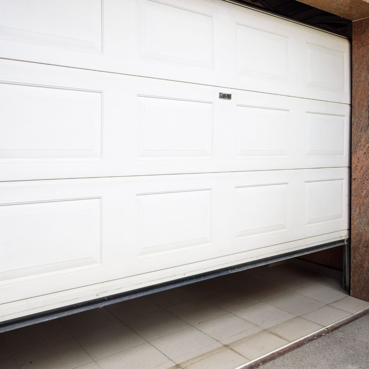 White garage door stuck half-open at the threshold—common sign your system needs inspection or repair
