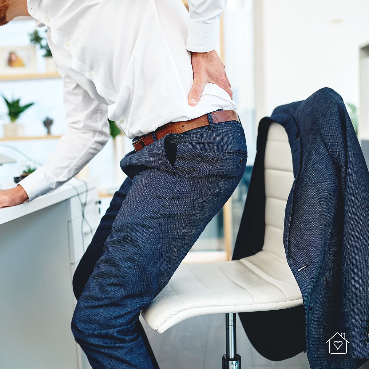 Man rising from desk chair while holding his lower back in pain.