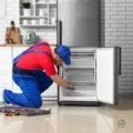 Appliance repair technician kneeling to service a refrigerator freezer in a modern kitchen