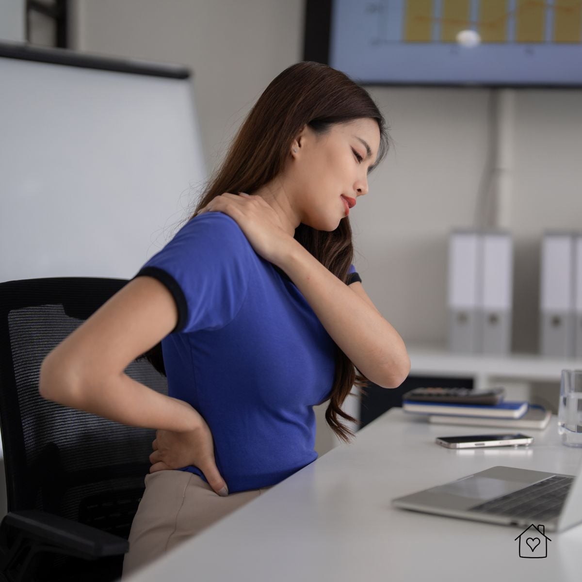 Woman at computer rubbing neck and lower back due to desk strain.