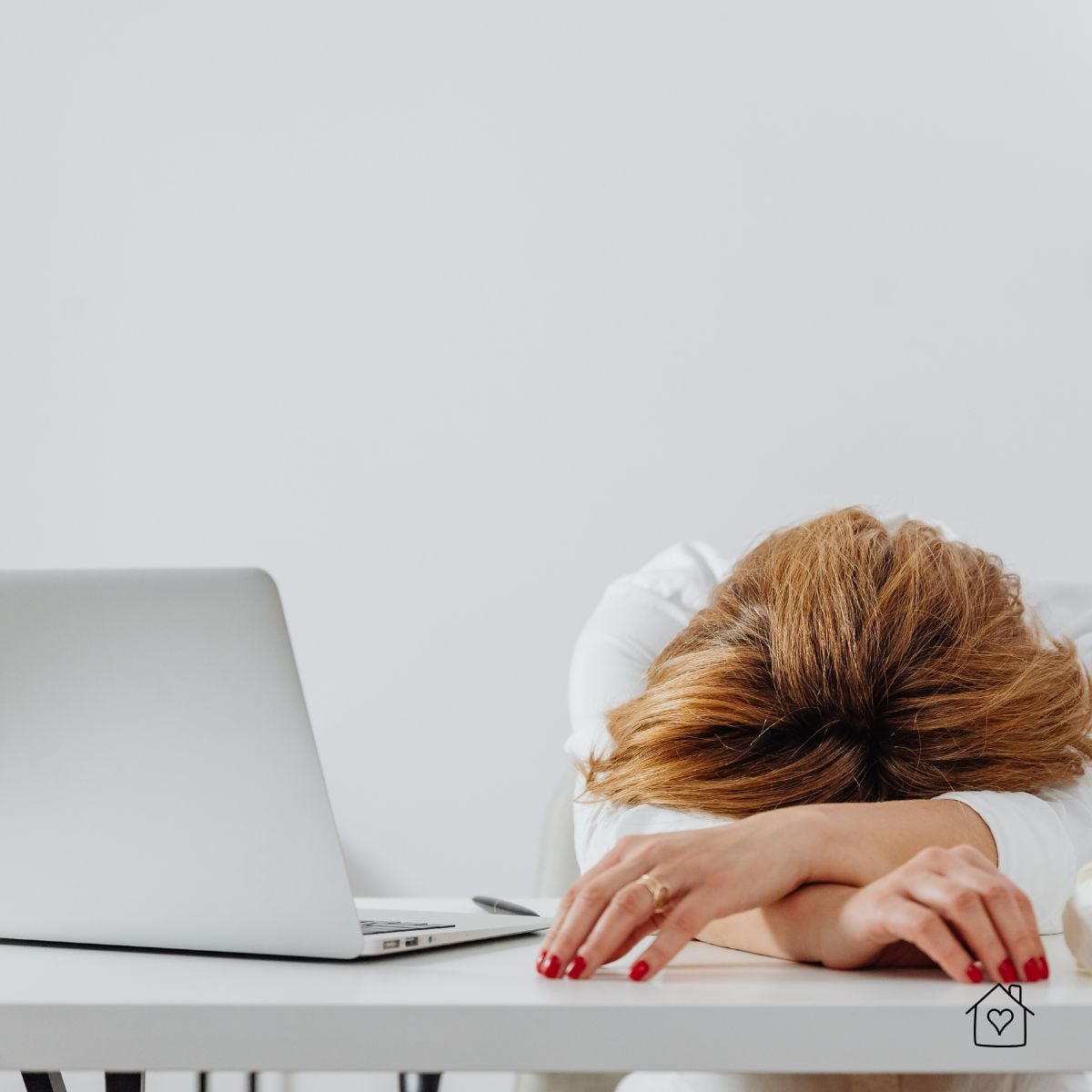 Tired worker with head on desk beside laptop, overwhelmed and fatigued.