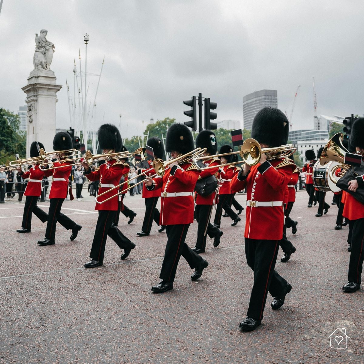 Soldiers in red uniforms and bearskin hats marching with brass instruments during the Changing of the Guard in London.