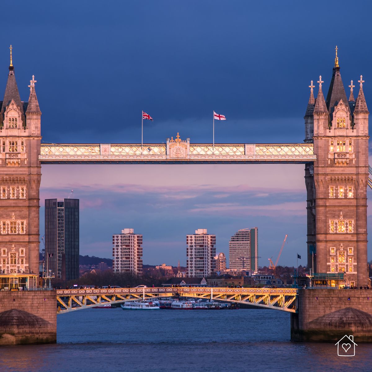 Tower Bridge glowing at dusk above the River Thames with the London skyline in the background.