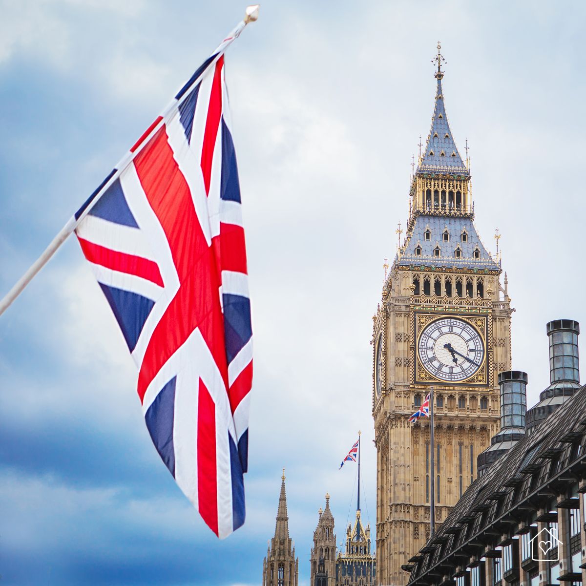 Union Jack flag waving in front of Big Ben and the Palace of Westminster on a cloudy London day.