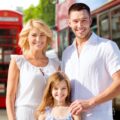 Smiling parents and daughter posing together on a London street with a red double-decker bus in the background.