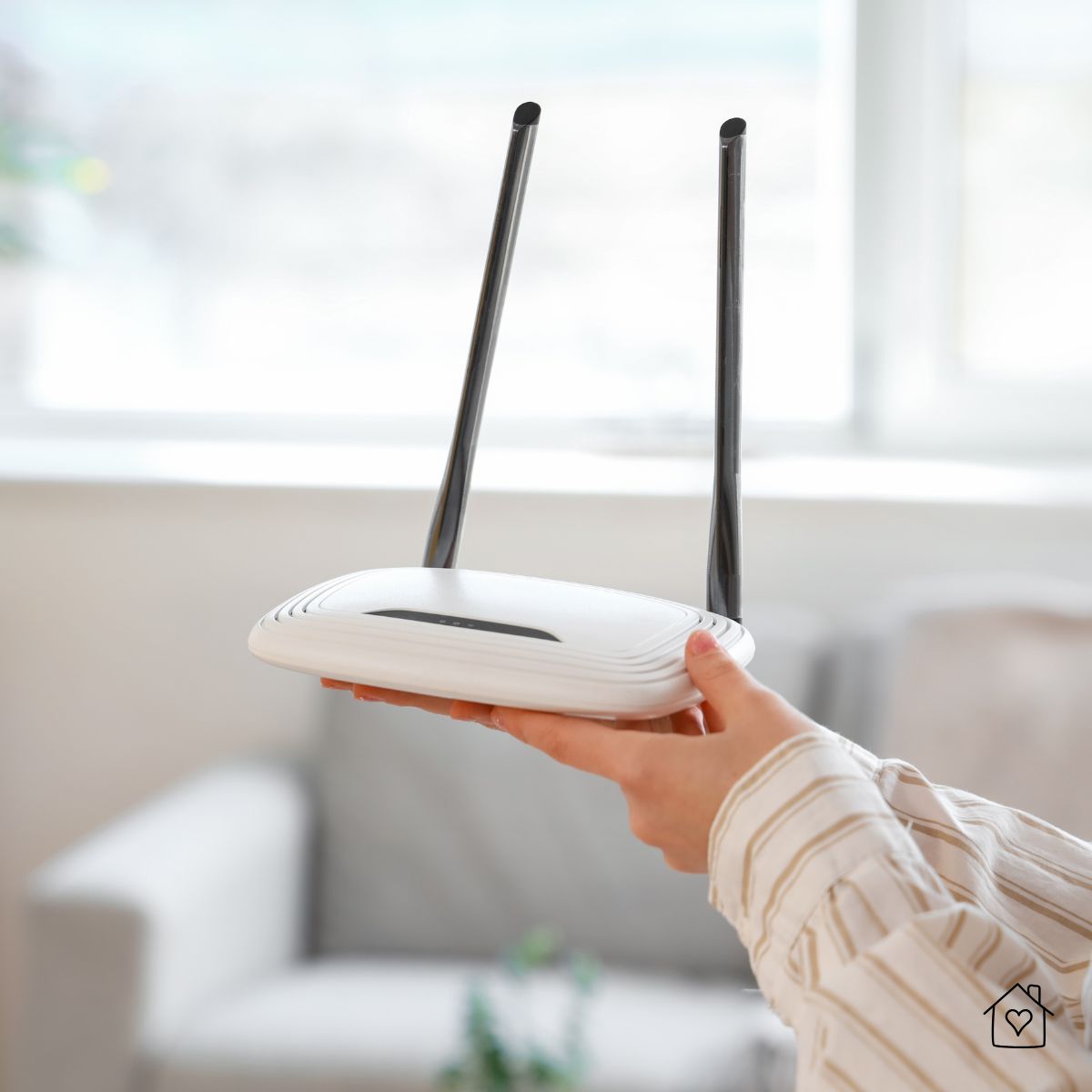 Person holding a modern wireless router with two antennas in a bright living room, preparing a home network for smart devices.