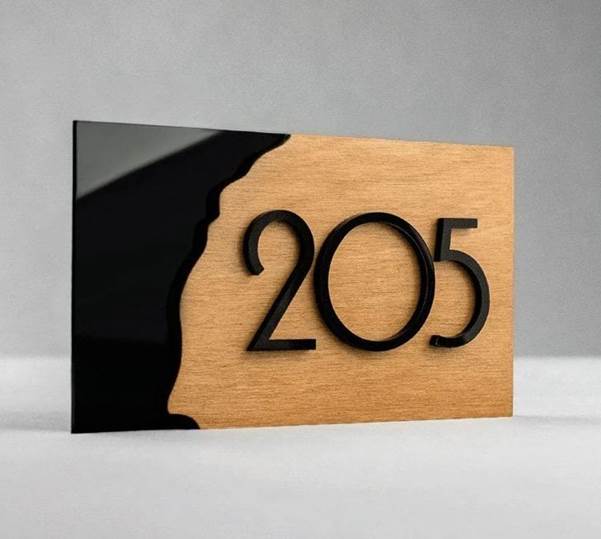 Modern mixed-material room plaque with a matte black section and a warm wood panel, mounted against a neutral wall