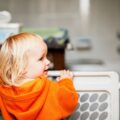Toddler standing behind a safety gate in a childproofed home.